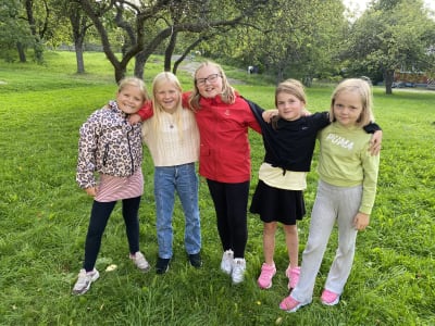Fem flickor i en trädgård.