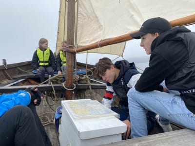 Fyra ungdomar åker allmogebåt och tittar på ett sjökort.