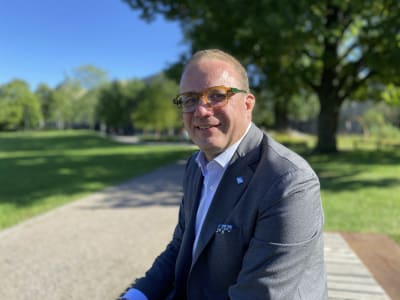 En porträttbild på en medelålders man i grå kostym och orangea glasögon. Han tittar in i kameran och ler.