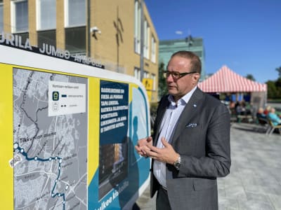 En man i grå kostym tittar på en karta som visar rutten för en framtida spårvagnsrutt. Han gestikulerar på ett sätt som visar att han förklarar något.