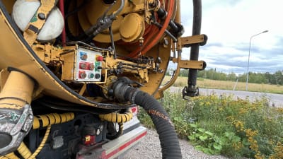 Bakdelen av en sugbil där röret och knapparna syns. Den står på en grusväg vid en äng.