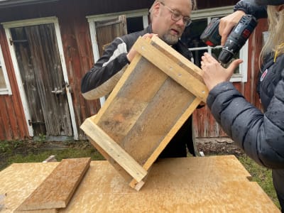Två personer bygger en fågelholk med hjälp av en borrmaskin.
