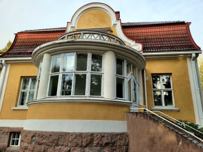 En gul och vit stenbyggnad med stora fönster.