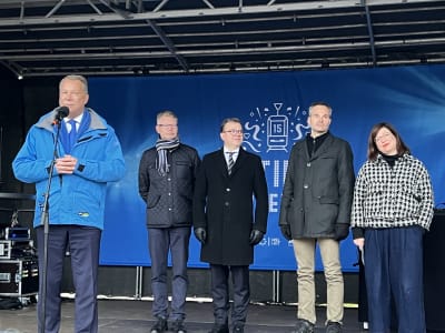 Esbo stadsdirektör Jukka Mäkelä håller tal, på scenen bakom honom står också politikerna Petteri Orpo, Annni Sinnemäki och Kai Mykkänen.