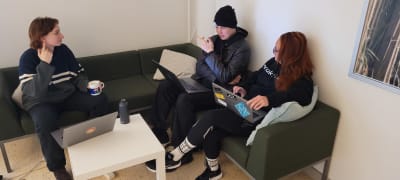 Två studerande sitter i en soffa och diskuterar med sin lärare