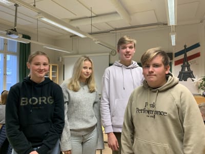 En grupp på fyra skolelever poserar på bild i klassrum, de är alla tonåringar, till vänster står två flickor och till höger två pojkar.