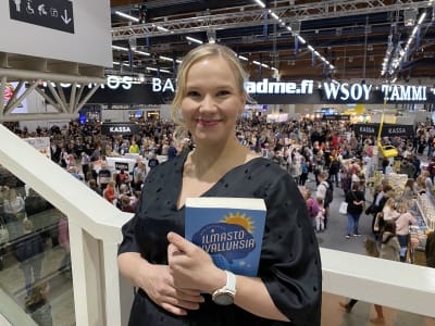 Mira Hulkkonen står med bok i famnen på Bokmässan i Helsingfors