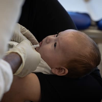Vauvaa katsoo terveydenhoitajaa, joka antaa hänelle rotavirusrokotteen.
