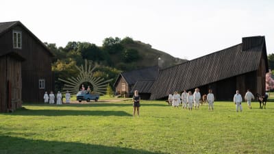 Dani (Florence Pugh) står mitt bland en massa svarta stockhus och några vitklädda människor. 