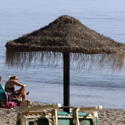 Två personer sitter i solstolar på stranden i Malaga.