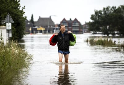 En man tar sig igenom en översvämmad gata i Arcen, Nederländerna.