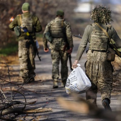 Kolme ukrainalaissotilasta kävelee kadulla Hersonin alueella selin kameraan.