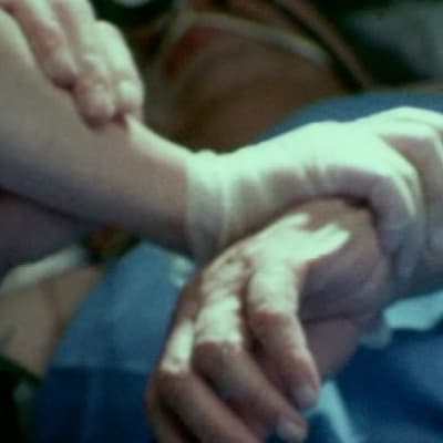 Sairaanhoitaja pitää vuoteessa makaavaa potilasta käsivarresta kiinni 1979