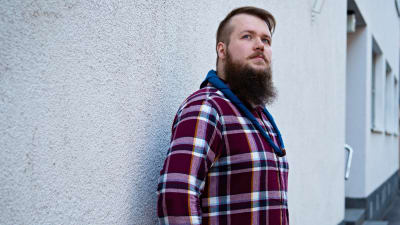 En ung man iklädd scouthalsduk står vid en vägg och blickar uppåt mot skyn.
