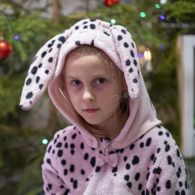 Tyttö katsoo kameraan. Takana joulukuusi, jossa on koristeita.