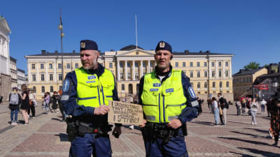 Två poliser står med ett plakat med antirasistiskt budskap.