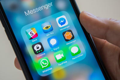 En ruta med olika appar (bland annat Whatsapp och Signal) på en telefonskärm. En hand håller i telefonen.