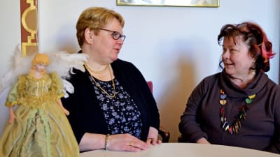 Diakonissorna Barbro Ollberg och Karin Salenius samtalar. Statyett föreställande ängel som dekoration på bordet framför dem.