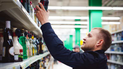 En man sträcker sig efter en flaska i en affärshylla.
