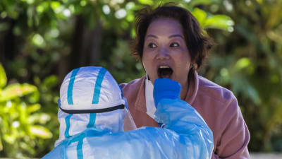 En person i munskydd tar ett coronatest på en kvinna.