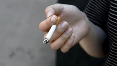 Hand som håller i en rykande cigarett.