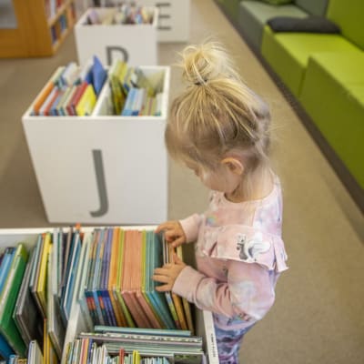 Ett barn bläddrar igenom barnböcker i ett bibliotek.