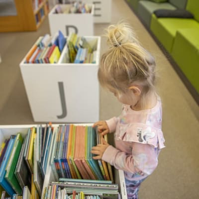 Ett barn bläddrar igenom barnböcker i ett bibliotek.