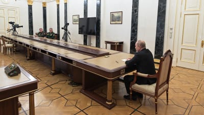 Rysslands president Vladimir Putin sitter vid en mycket långt bord i ändra ändan sitter två generaler