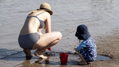 Vuxen och barn i solhatt vid strand. 