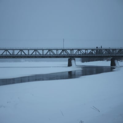 Talvinen maisema sillasta ja osittain sulana olevasta joesta. 