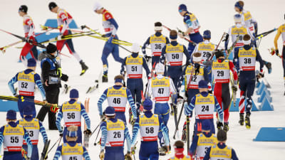 Skidåkare springer med skidor i händerna mot start.