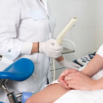 En gynekolog håller i en ultraljusstav. En kvinna sitter i gynekologstol bredvid.