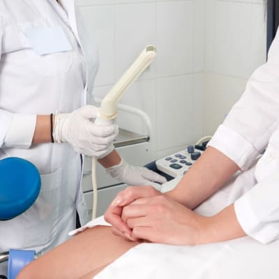 En gynekolog håller i en ultraljusstav. En kvinna sitter i gynekologstol bredvid.