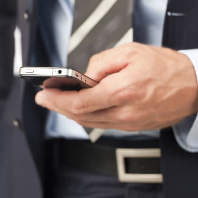 En man i kostym håller en telefon i sin hand