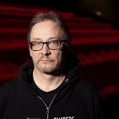 Mies seisoo elokuvateatterin punaisten penkkirivien edessä ja katsoo kameraan. Yllään hänellä on Tampere Film Festivalin huppari.
