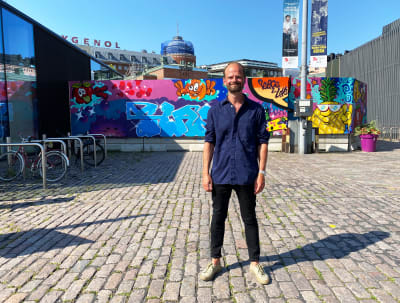 Ville Relander står framför en graffitimålad trävägg som täcker in Hagnäs saluhall.