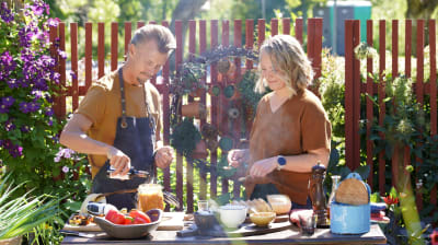 En man och en kvinna som står i ett somrigt utekök och lagar en grillsås.