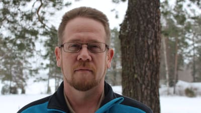 Jesper Sunström i uteomhusmiljö, snö och och tallar i bakgrunden, i blå fleecejacka