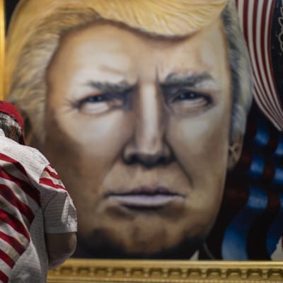 Man i fägrgglad skjorta med USA-flagga beundrar tavla av Donald Trump.