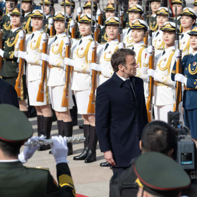Kiinan Xi on kääntyneenä kuvassa vasemmalla, Ranskan Macron oikealle kiinalaisten naissotilaiden rivistöjen edessä. Kummallakin on vakava ilme.