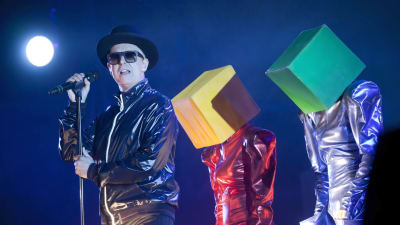 Pet Shop Boysin Neil Tennant ja laatikkopäitä lavalla.