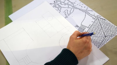 EN hand som håller en penna och ritar upp en skiss av en detaljplan.