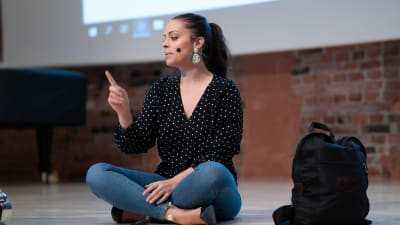 Felicia Margineanu sitter på scengolvet med benen i kors under en föreläsning om unga och självkänsla.