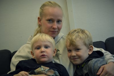En kvinna med sina två söner lér in i kameran.