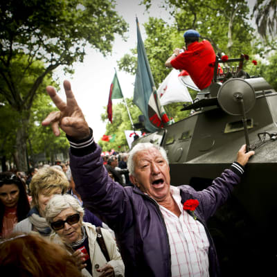 En man gör victorytecknet framför en av fordonen som hade använts i nejlikerevolutionen