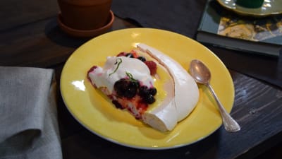 Ett gult fat med en portion av en marängtårta. Tårtan är fylld med grädde och bär.
