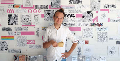 Wesa Aapro, mies valkoisessa paidassa vasten seinää jolla piirroksia.