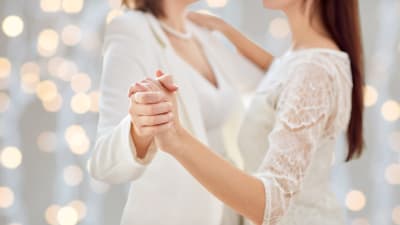 Kvinnligt par i brudklänning dansar i sidoprofil.