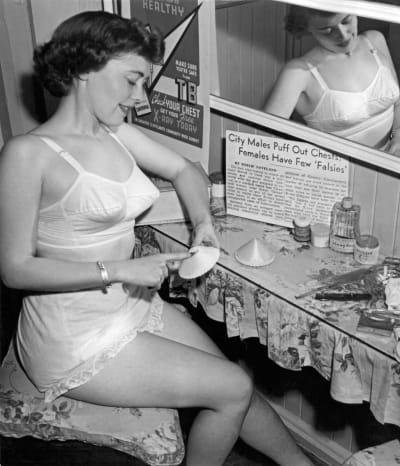 Ena kvinna år 1949 som tittar på sina behåinlägg för att få strutformen på brösten.