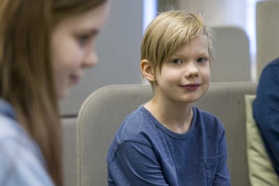 Lauritsalan koulun 3.-luokkalainen Aleksi Liutu istuu koulun oleskelutilassa ja katsoo kameraan. 